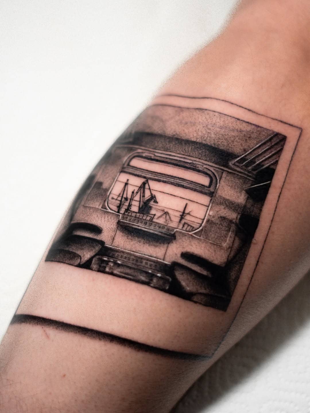 Tatuaż surrealistyczny przedstawiający widok portu i żurawi stoczniowych przez okno samochodu, wykonany przez Nava w Sztorm Tattoo Gdańsk, na przedramieniu mężczyzny.