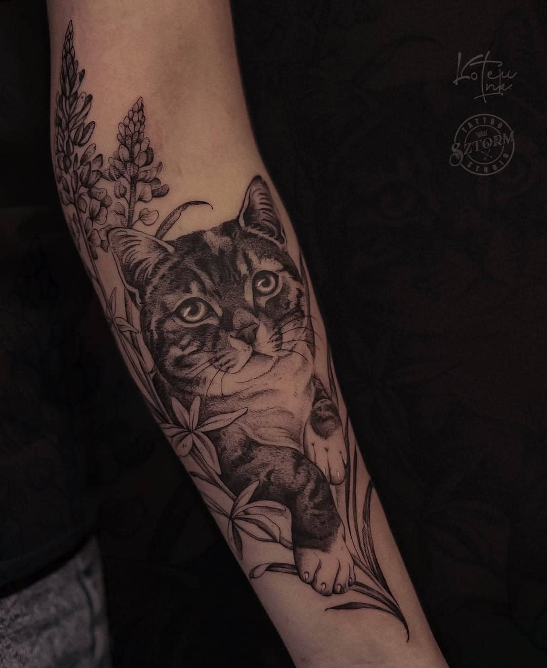 Realistyczny tatuaż kota w otoczeniu kwiatów i liści, autorstwa Kotetu w Sztorm Tattoo Gdańsk.