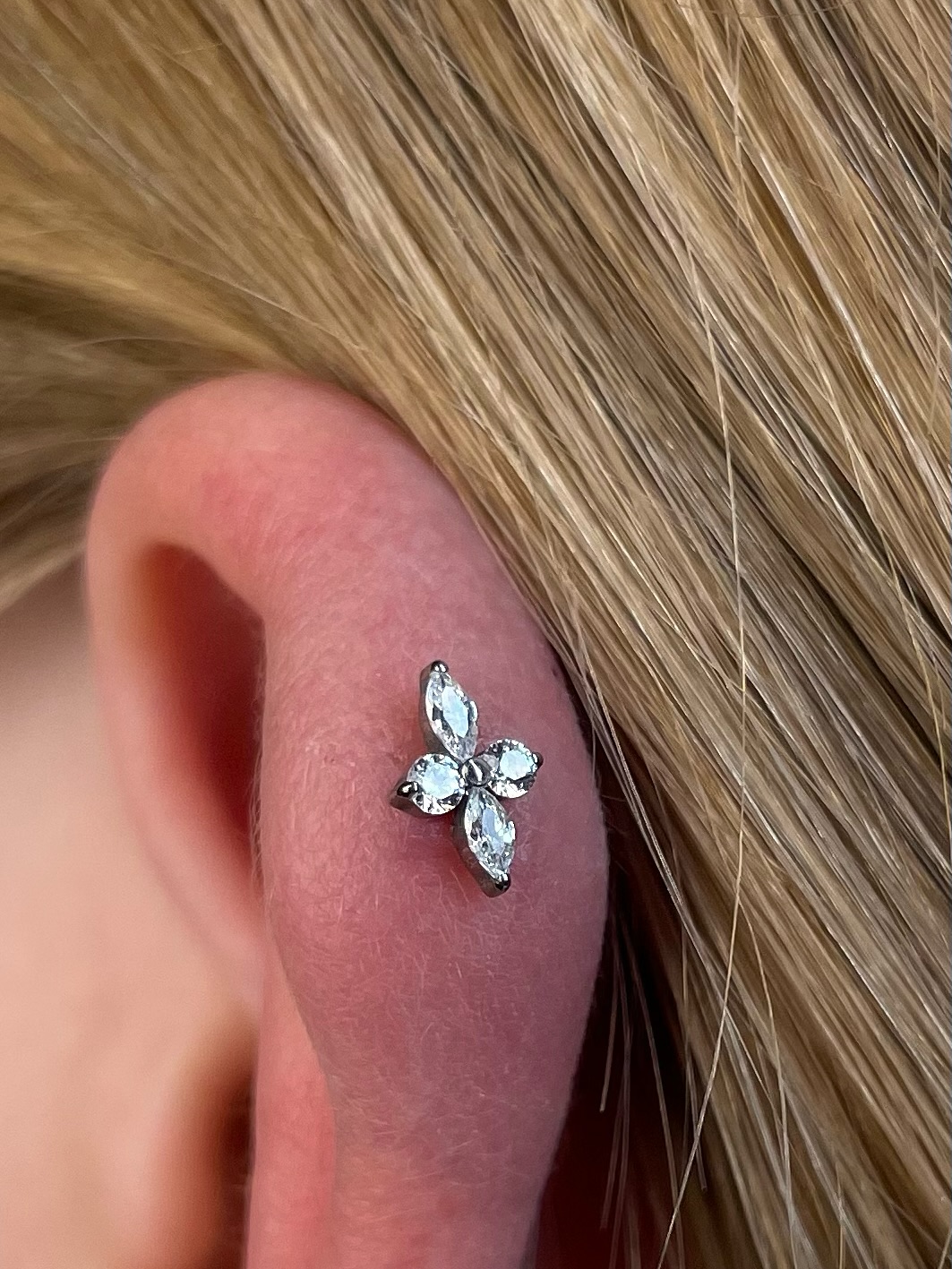 Ucho z kolczykiem przypominającym kwiat z czterech przezroczystych kamieni w kształcie marquise.